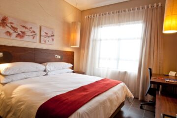 Classic King bed beneath botanical artwork with sheer-curtained window at Metcourt Umfolozi, Empangeni