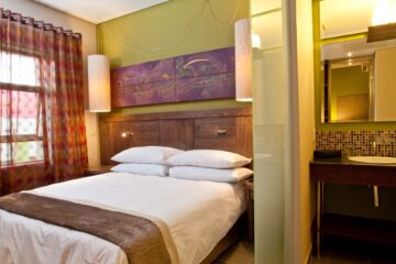 Executive Suite bedroom with green accent wall, artwork and open-plan vanity at Metcourt Umfolozi, Empangeni